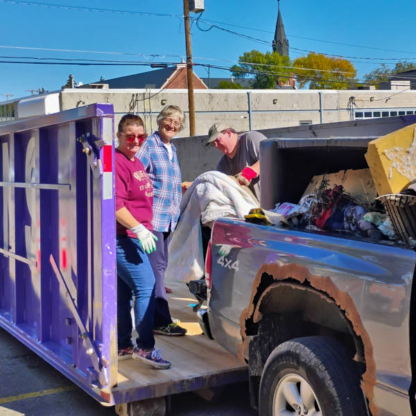 three volunteers emptying garbage from truck to bin